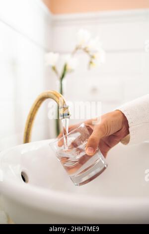 Nahaufnahme der Hand einer Frau, die in einem alten Badezimmer ein Glas mit Wasser füllte Stockfoto