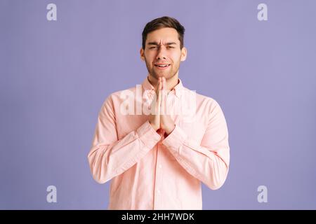 Porträt von aufgeregt jungen Mann hält die Hände gefaltet im Gebet betteln über etwas machen Wunsch halten die Daumen gekreuzt auf rosa isolierten Hintergrund im Studio, Stockfoto