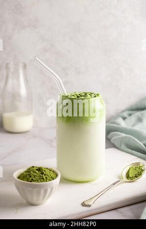 Kalte Milch und geschlagene Matcha mit Eiern oder Rahm, Glas Dalgona Matcha Latte und Löffel Grüntee-Pulver auf weißem Hintergrund. Stockfoto