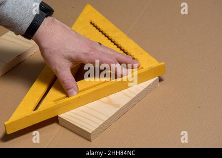 Zimmermann, der ein altes Quadrat verwendet, um eine diagonale Linie auf einem Holzbrett zu markieren Stockfoto