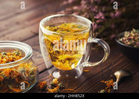 Glas Tasse gesunden Calendula Kräutertee, Glas getrocknete Calendula Heilkräuter und Heidekraut Blumen auf Holztisch. Alternative Kräutermedizin. Stockfoto