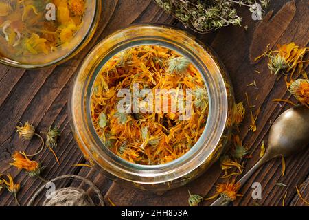 Glas mit getrockneten Ringelblumenblüten, Tasse gesunden Ringelblume Kräutertee, Thymian Heilkräuter auf Holztisch. Draufsicht. Alternative pflanzliche Arzneimittel Stockfoto