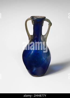 Glasflasche mit zwei Griffen (Amphoriskos) 1st. Jahrhundert n. Chr. römisch Durchscheinend streifendes Kobaltblau; Griffe in lichtdurchlässigem hellblaugrün.Bördelrand, mit abgeschrägter Außenlippe; zylindrischer Hals, der sich nach unten ausdehnt und mit einem länglichen Kugelkörper verschmilzt; kleiner, konkaver Boden; Zwei zweirippige Griffe, die an der Basis des Halses angebracht wurden, mit nach unten ausstreckenden Krallen, die nach oben gezogen und nach außen gezogen wurden, dann eingebogen und auf die Unterseite des Randes und die Oberseite des Halses gedrückt wurden. Gebrochen und repariert um den Unterkörper herum, mit drei Löchern an der Seite; mehrere glasige Einschlüsse, darunter ein großer Fleck in einem Griff; Braune, emaillierte Flecken Stockfoto