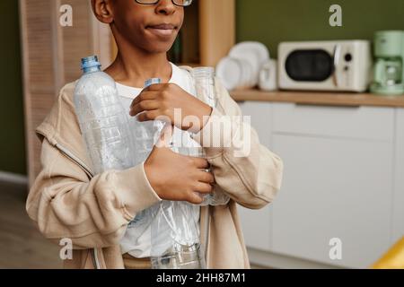 Eine kleine Aufnahme eines Jungen im Teenageralter, der Plastikflaschen hält, während er Hausmüll zu Hause sortiert und Platz kopiert Stockfoto