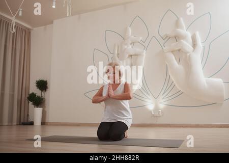Die ganze Aufnahme einer eldeligen Frau, die eine namaste Geste machte und auf ihrer Yogamatte meditierte Stockfoto
