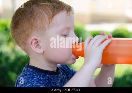 Ein rothaariger 4-jähriger Junge trinkt aus der Nähe Wasser aus einer Flasche. Ein Kind trinkt an einem heißen Sommertag Wasser aus einer Flasche. Stockfoto