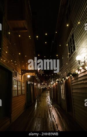 Enge Straße zwischen Bryggen an den zum UNESCO-Weltkulturerbe gehörenden Docks in Bergen. Nachts mit Weihnachtsschmuck Stockfoto