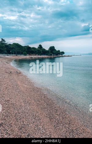 Leerer Strand am Meer in der Stadt Crikvenica, Kroatien. Früher Sommermorgen mit bewölktem Himmel. Stockfoto