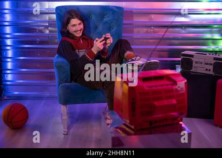 Millennial Mann im Retro-Stil genießen und spielen Retro alte Video-TV-Spiel in Neon-Interieur Stockfoto