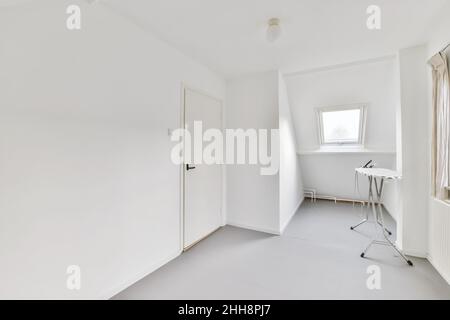 Bügeleisen steht auf dem Bügelbrett in der Nähe des Fensters im weißen Bügelzimmer Stockfoto