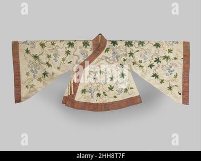 Theaterjacke mit Weinreben 18th Century China das Muster dieser Jacke – Teil eines Theaterkostüms mit Rock 30.76.23 – zeigt ein Amalgam aus Weinreben und Drachen, das sich über den weißen Hintergrund dreht und sich winkt. Auf der linken Seite der Jacke ist ein Drachenkopf zu sehen, und ein anderer befindet sich in der Mitte auf dem Rücken. Die Qualität sowohl der Materialien als auch der Verarbeitung ist sehr hoch: Man beachte die subtilen Farbveränderungen der Seidenstickerei innerhalb der Blätter und die Verwendung von Goldfäden zur Abgrenzung der Zweige, Blätter und Ranken der Weinrebe. Theaterjacke mit Grapev Stockfoto