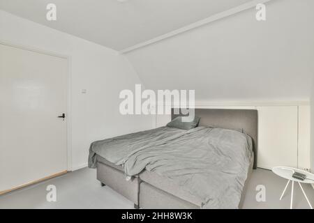 Weißes, modernes Schlafzimmer mit einem grauen Doppelbett und weißen Wänden Stockfoto