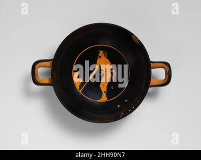 Terrakotta-Kylix (Trinkbecher) ca. 460–450 v. Chr. dem Euaion-Maler Interior zugeschrieben, Satyr-KochnObwohl Satyr-Ikonographie tendenziell auf die spezifischen Aktivitäten von Dionysos, dem gott des Weins, und seinen Anhängern konzentriert, werden Satyrs gelegentlich in menschliche Rollen gegossen. Die Mahlzeit des Satyrs ist in einem Skyphos (tiefer Trinkbecher) enthalten, der auf einer Stütze von unbestimmter Form steht. Mit dem Stock in der linken Hand scheint er ein Feuer unter der Stütze zu schüren. Terrakotta-Kylix (Trinkbecher) 247340 Stockfoto