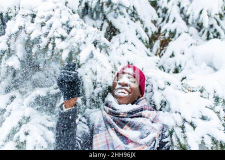 afroamerikanischer Handsom-Mann in rotem Hut und stilvollem karierten Mantel Blick auf die Kamera mit toothy schneeweißen Lächeln im Freien im Park Stockfoto