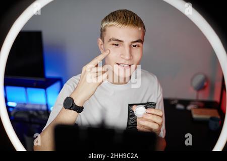 Vorderansicht Porträt des blonden jungen Mannes, der männliche Hautpflege-Tutorial mit Ringlicht filmt, Kopierraum Stockfoto