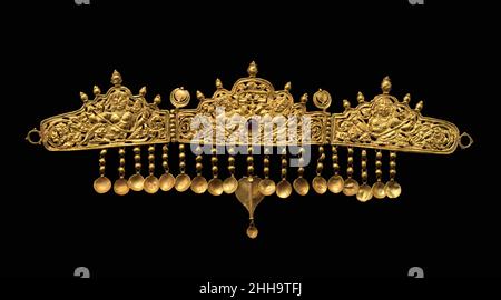 Diadem with Kinnaris (Half-Bird, Half-Female Creatures) 9th–10th Century India (Jammu & Kashmir, antikes Königreich Kaschmir) Dieses dreiteilige Diadem ist ein seltenes Beispiel für frühen indischen Schmuck. Vier Kinnaris – halb-Vogel, halb-weibliche himmlische Zelebranten – dominieren das Design. Es wurde wahrscheinlich in Kaschmir gemacht, nach dem Abbild der Kinnaris zu denen zu urteilen, die auf dem Tempel des Avantisvamin aus dem 9. Jahrhundert in Avantipur, Kaschmir, dargestellt wurden. Diadem mit Kinnaris (Halbvogelwesen, Halbweibchen). Indien (Jammu & Kaschmir, altes Königreich Kaschmir). 9th–10th Jahrhundert. Goldinsatz mit Granat. Schmuck Stockfoto