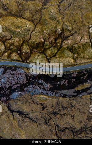 Eine Luftaufnahme zeigt eine Straße, die durch atemberaubende texturierte Landschaften in khaki-Grün, Braun und Schwarz führt, so ungewöhnlich, dass sie fast nicht real aussehen. Stockfoto