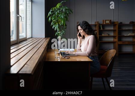 Lächelnde Unternehmerin im Gespräch mit dem Kunden über das Handy, mit Online-Bestellung auf dem Laptop arbeiten Stockfoto