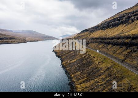 Ein einmotorisches Wohnmobil fährt an dramatischen Klippen und schimmerndem Wasser vorbei in einen dunklen, wolkigen Himmel. Stockfoto