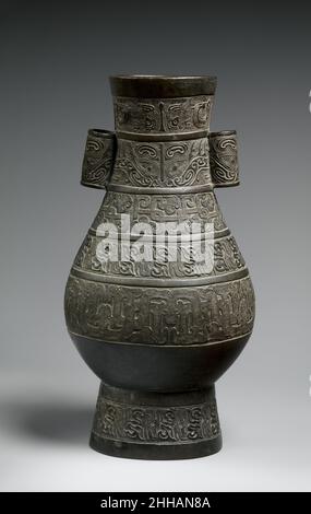 Vase mit archaistischem Design 14th Century China Diese birnenförmige Vase hat einen breiten ovalen Mund, einen langen Hals mit zwei röhrenförmigen Griffen, einen anschwellenden Bauch und einen hohen Ringfuß. Seine Oberfläche ist mit sechs horizontalen Bändern archaistischer Motive verziert, fünf am Körper und eines am Fuß. Das obere Band besteht aus Vogel-ähnlichen Motiven in niedrigem Relief auf einem Hintergrund aus kleinen eckigen Spiralen. Die nächste enthält zwei Masken von fantastischen Tieren, die offenbar von alten Bronzedesigns abgeleitet sind, die sich auch auf der Oberfläche der Griffe wiederholen. Die dritte Band besteht aus verschachtelten „Dragons“ mit vage Stockfoto