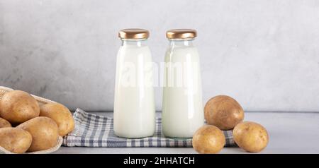 Vegane Milch auf pflanzlicher Basis in zwei Flaschen. Alternative Kartoffelmilch und Kartoffelknollen auf grauem Tisch Stockfoto