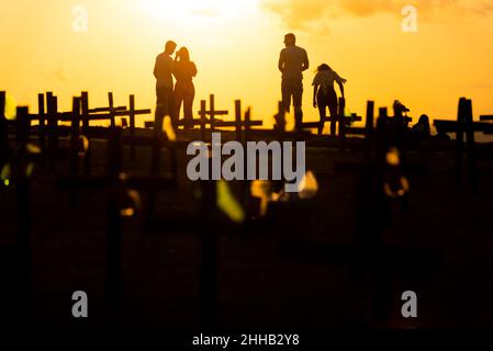 Silhouette von Menschen und Kreuzen, die auf dem Boden zu Ehren der von Covid-19 Getöteten befestigt sind. Sonnenuntergang in Salva Stockfoto