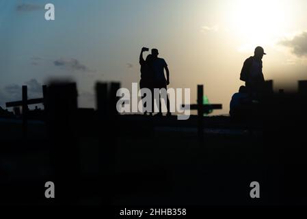 Silhouette von Menschen und Kreuzen, die auf dem Boden zu Ehren der von Covid-19 Getöteten befestigt sind. Sonnenuntergang in Salva Stockfoto