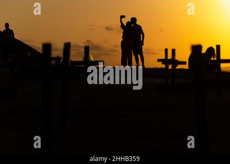 Silhouette von Menschen und Kreuzen, die auf dem Boden zu Ehren der von Covid-19 Getöteten befestigt sind. Sonnenuntergang in Salva Stockfoto