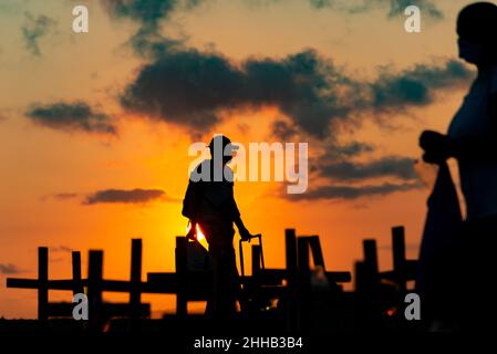 Silhouette von Menschen und Kreuzen, die auf dem Boden zu Ehren der von Covid-19 Getöteten befestigt sind. Sonnenuntergang in Salva Stockfoto