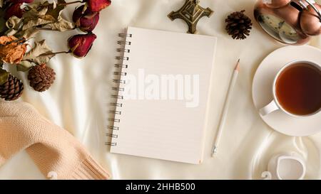 Draufsicht, femininer Arbeitsplatz-Hintergrund mit leerem Spiral-Notizbuch, Teetasse, Vintage-Uhr, getrockneten Blumen und Pullover auf weißem Hintergrund. Winter, aut Stockfoto