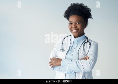 Afroamerikanische Ärztin im Gesundheitswesen mit gekreuzten Armen auf grauem Porträt Stockfoto