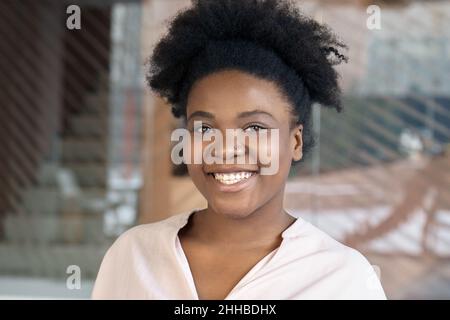 Die junge afroamerikanische Frau lächelt und schaut sich das Nahaufbildnis der Kamera an Stockfoto