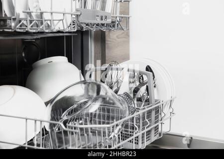 Frontansicht der offenen automatischen Edelstahl-Einbaumaschine mit vollständig integrierter Top-Control-Spülmaschine mit sauberen Utensilien, Besteck, Gläsern, Geschirr, Tellern in der modernen Wohnküche Stockfoto