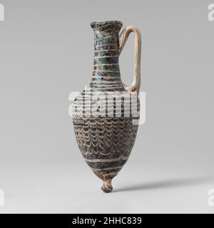 Glas Amphoriskos (Parfümflasche) 1st. Jahrhundert v. Chr. Griechisch, zypriotisch Durchscheinendes Grün, schwarz erscheinend; Griffe und Sockel von unsicherer Farbe; Patch in der Nähe der Basis in opakes Rot; Trail in opakes Weiß.nach innen abfallende Randscheibe, mit nach oben gerundeter Lippe; zylindrischer Hals, sich nach unten ausdehnend; schräge Schulter mit eingerückter Oberfläche; piriformer Körper; aufgesetzter Knopfsockel; Zwei Stangengriffe, die in Pads über die Schulter aufgetragen wurden, vertikal nach oben gezogen, dann nach innen und unten geloopt und über die Traildekoration auf den Hals unter dem Rand gedrückt wurden.eine weiße Spur wird auf die Kante des Randes aufgetragen und dann spiralförmig um Hals und Schulter gewickelt Stockfoto