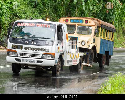 Bergungs-LKW, der an einem regnerischen Tag in der Nähe von Kandy in Sri Lanka einen abgebrochenen Ortsbus auf einen Hügel schleppt. Stockfoto