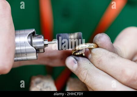 Nahaufnahme Hände des Handwerkers Juwelier Polieren einer goldenen Ring-Oberfläche mit Schleifmaschine. Der Goldschmied arbeitet gerade. Stockfoto