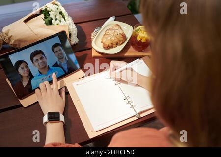 Geschäftsfrau, die den Planer füllt Wenn Sie während eines Online-Meetings zu Kollegen gehen, schauen Sie über die Schulter Stockfoto