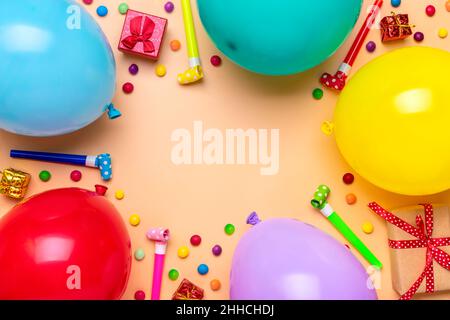 Farbenfroher Partyrahmen mit roter Geschenkbox mit verschiedenen Party-Konfetti, Luftballons, Luftschlangen, Pokern und Dekorationen auf beigem Hintergrund. Urlaubskarte flach Stockfoto