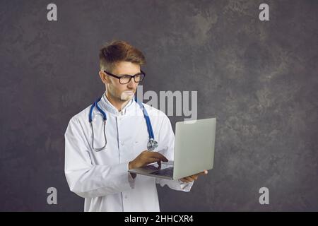 Porträt eines selbstbewussten jungen männlichen Hausarztes, der für seine Arbeit einen Laptop verwendet. Stockfoto