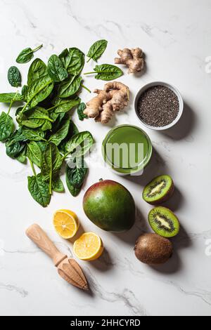 Grüner Spinat und Mango-Smoothie im Glas mit Zutaten auf weißem Marmorboden, Draufsicht. Entgiftungsgetränke-Konzept. Stockfoto