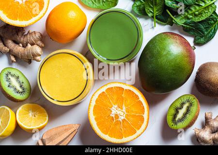 Gelber Mango-Smoothie und grüner Spinat-Smoothie in Gläsern mit Zutaten auf weißem Marmorboden, Nahaufnahme. Entgiftungsgetränke-Konzept. Stockfoto