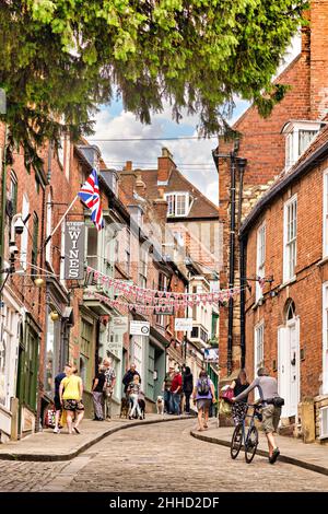 2. Juli 2019: Lincoln, UK - Menschen gehen und besichtigen in Steep Hill, der berühmten mittelalterlichen Straße der Stadt. Ein Mann schiebt ein Fahrrad den Hügel hinauf. Stockfoto