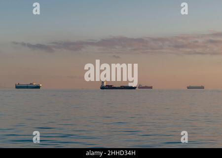 Vier große Containerschiffe segeln im Abendlicht auf der Horizont-Linie Stockfoto