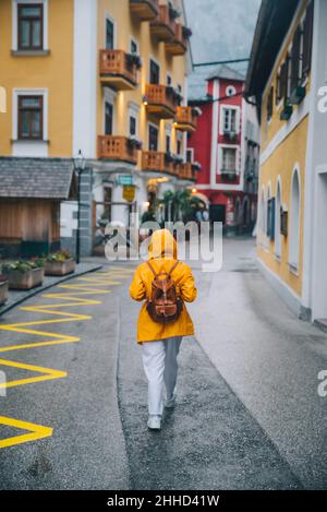 Frau in gelbem Regenmantel beim Spaziergang durch die hallstätter Straßen regnerisches Wetter Stockfoto