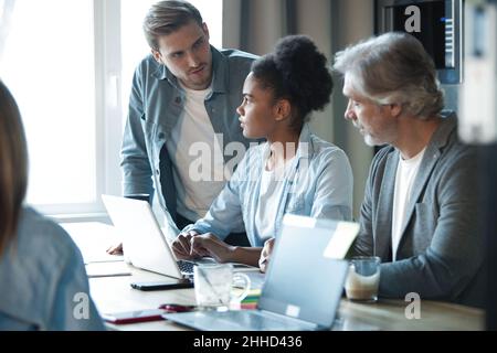 Lächelnde Kollegen treffen sich in einem Brainstorming in der Vorstandsetage und diskutieren gemeinsam Finanzstatistiken, glückliche, multirassische Mitarbeiter haben Spaß an der Zusammenarbeit Stockfoto