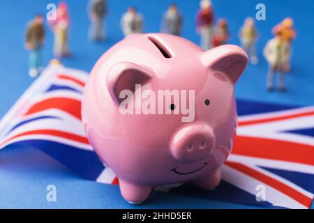 Sparschwein, Fahne und Plastikspielzeug Menschen auf farbigem Hintergrund, ein Konzept zum Thema Einkommen in Großbritannien Stockfoto