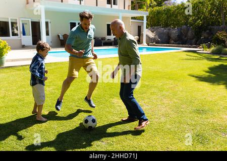 Kaukasischer Großvater, Vater und Sohn spielen gemeinsam im Garten Fußball Stockfoto