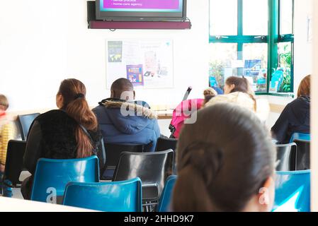 Verschiedene Menschen, die in einem OP-Wartezimmer eines Arztes sitzen und darauf warten, von einem Arzt oder einer Krankenschwester in einer geschäftigen Situation gesehen zu werden Stockfoto