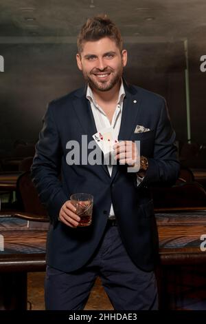 Erfolgreicher Mann mit zwei Assen in der Hand feiert Pokergewinn mit einem Glas Brandy Stockfoto