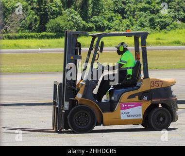 Air Niugini Ramp Services Mitarbeiter in Sicherheitsausrüstung fährt einen gelben Gabelstapler auf dem Asphalt am Flughafen Madang. Stockfoto